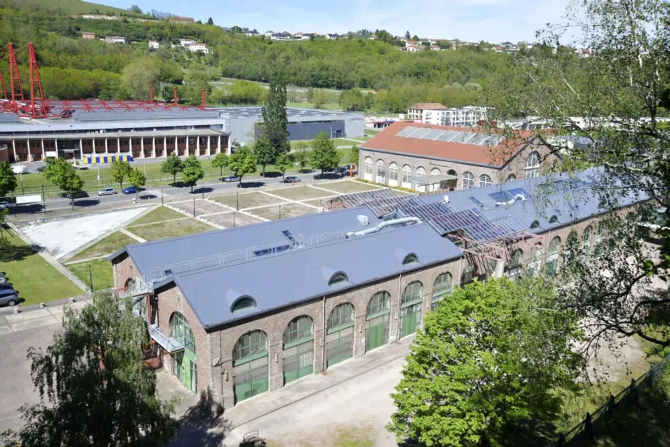Une vue aérienne lumineuse du campus moderne de l'IUT du Creusot entouré d'arbres et de verdure sous un ciel bleu clair, avec des étudiants marchant sur les allées.