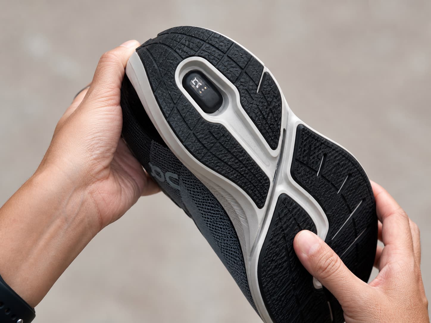 Mains inspectant une chaussure connectée retournée, semelle et module visibles.