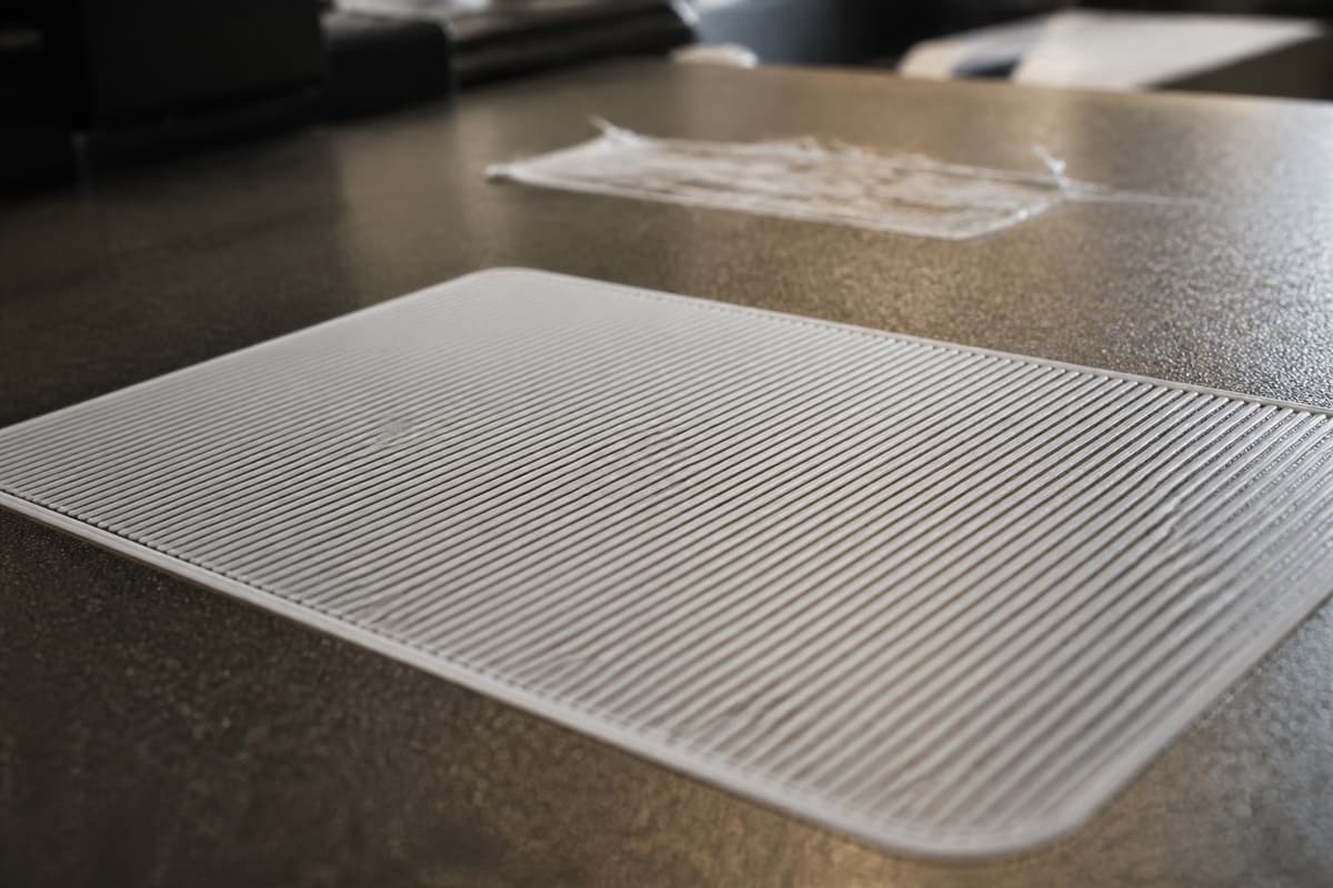 Gros plan sur un plateau d'imprimante 3D montrant des lignes de première couche bien régulières au premier plan et une zone discrète de décollement en arrière-plan.