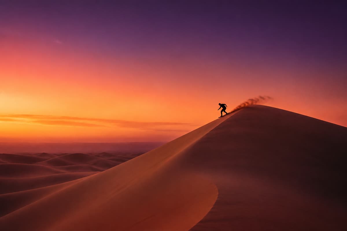 Silhouette d'un surfeur des sables glissant sur une haute dune dorée au coucher du soleil dans un désert vaste et épuré.